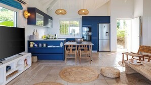 A modern kitchen with blue cabinets, a dining area with wicker chairs, and a large TV. - Sunset view, beach walk, heated pool (SAINT MARTIN)