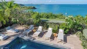 A poolside area with lounge chairs and a view of the sea. - Sunset view, beach walk, heated pool (SAINT MARTIN)