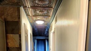 Un couloir doté d’un plancher en bois, d’un plafond orné de motifs et d’un rideau bleu au fond.