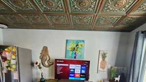 Une pièce comprenant une table à manger en bois, un téléviseur fixé au mur, un réfrigérateur et un plafond décoratif.