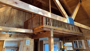 A wooden interior with a loft-style balcony, exposed beams, and a kitchen area with cabinets and a microwave. - Charming 3-bedroom + loft log cabin at Lake Bomoseen in Castleton, VT. Sleeps 12 (Fair Haven)