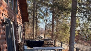 A wooden deck with Adirondack chairs, picnic tables, and a grill. - Charming 3-bedroom + loft log cabin at Lake Bomoseen in Castleton, VT. Sleeps 12 (Fair Haven)