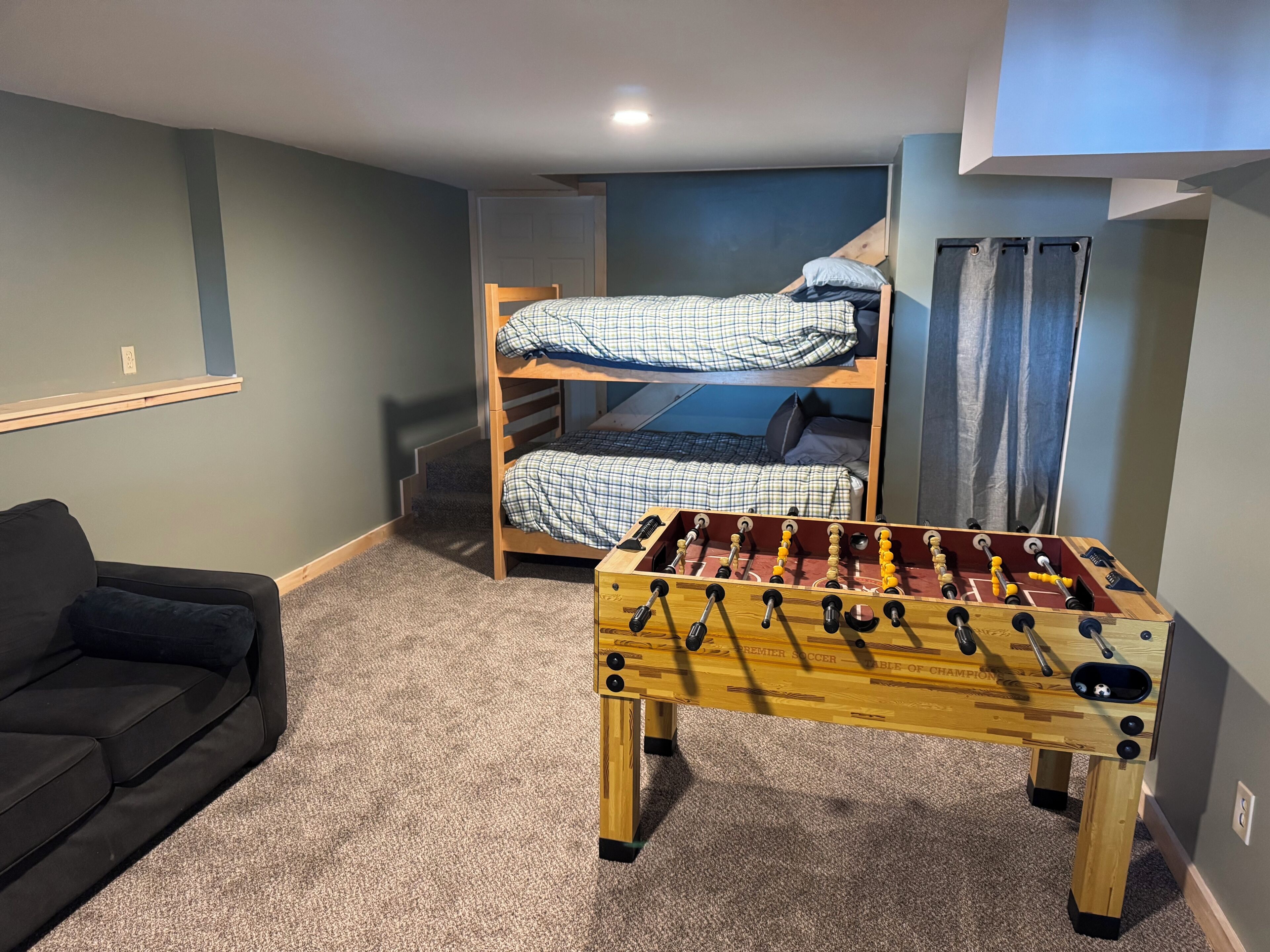 A room with a bunk bed, a sofa, and a foosball table.
