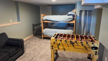 A room with a bunk bed, a sofa, and a foosball table.