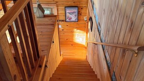 A wooden staircase with a metal handrail, wooden walls, and a framed picture on the wall. - Charming 3-bedroom + loft log cabin at Lake Bomoseen in Castleton, VT. Sleeps 12 (Fair Haven)