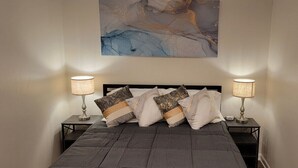 Ein Schlafzimmer mit einem großen Bett, zwei Nachttischen mit Lampen und einem an der Wand hängenden abstrakten Gemälde.
