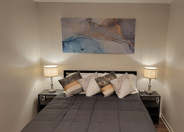 A bedroom with a large bed, two bedside tables with lamps, and a wall-mounted abstract painting. - Beautiful Studio Apt 6 -Down Stairs (Baton Rouge)