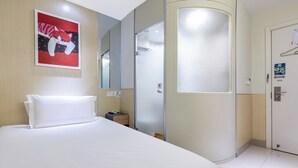 Una camera d'albergo con un letto, un comodino, uno specchio, una porta con pannello in vetro satinato e un'opera d'arte appesa al muro raffigurante un gatto.