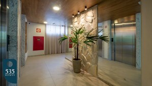 A modern elevator area with a potted plant, a red emergency box, and a sign indicating the elevator's location. - Stay in a Condo near Shopping da Bahia (Salvador)