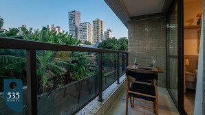 A balcony with a view of tall buildings, a glass railing, and a table with chairs. - Stay in a Condo near Shopping da Bahia (Salvador)