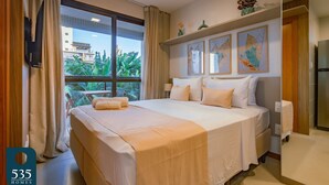 A hotel room with a large bed, a TV mounted on the wall, and a window with curtains. - Stay in a Condo near Shopping da Bahia (Salvador)