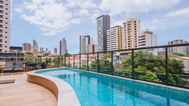 A rooftop swimming pool with a cityscape view, surrounded by greenery and modern buildings. - Stay in a Condo near Shopping da Bahia (Salvador)