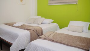 Two single beds with white bedding and brown throw blankets, a wooden bench, and a green wall with a window. - Vacation apartment (Cartagena de Indias)