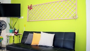 A black leather sofa with three pillows against a bright green wall, a mounted TV, and a decorative lattice. - Vacation apartment (Cartagena de Indias)
