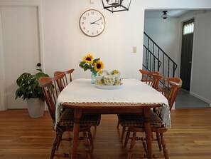 A dining area with a wooden table, four chairs, a clock on the wall, and a staircase in the background.