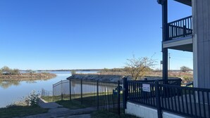 Un bâtiment doté d’un balcon donnant sur une étendue d’eau calme, d’une zone délimitée par une clôture et d’un panneau d’avertissement concernant la présence de caméras de surveillance.