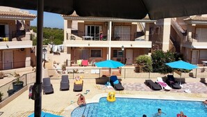 Ein Poolbereich mit Liegestühlen und Sonnenschirmen, umgeben von mehrstöckigen Gebäuden mit Balkonen.