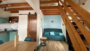 Ein gemütliches Zimmer mit einer Holztreppe, einem Bett mit türkisfarbenem Bettzeug, einem kleinen runden Tisch und einer Küchenzeile mit türkisfarbenen Schränken.