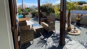Eine Terrassengaststätte mit Korbmöbeln, einem Glastisch und einem kleinen Gartenbereich mit einer Palme und einem Leuchtturmmodell.