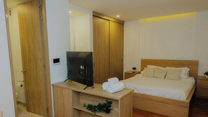 A bedroom with a wooden bed, a TV on a wooden stand, and a small shelf with a plant. - Suitable with terrace and coworking in downtown Candelaria, meters away from Chorro de Quevedo. (Bogotá)