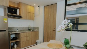 A modern kitchen with wooden cabinets, a stainless steel refrigerator, and a microwave. There is a dining table with two woven placemats and a potted orchid. - Suitable with terrace and coworking in downtown Candelaria, meters away from Chorro de Quevedo. (Bogotá)