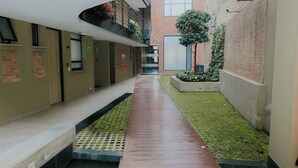 A narrow corridor with a wet floor, a brick building on the right, and a green area with plants. - Suitable with terrace and coworking in downtown Candelaria, meters away from Chorro de Quevedo. (Bogotá)