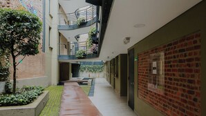 A multi-level corridor with a brick wall on the right, a wet floor, and a tree on the left. - Suitable with terrace and coworking in downtown Candelaria, meters away from Chorro de Quevedo. (Bogotá)