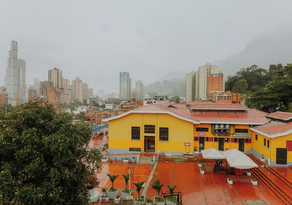 A yellow building with a red roof, surrounded by trees and a cityscape in the background.