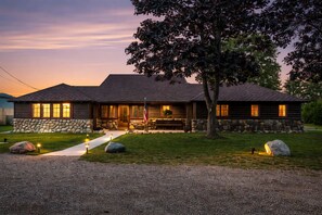 A log cabin with a stone foundation, a front porch, and a flagpole. - Lake Huron Beachfront, Hot Tub, Kayaks, 10 minutes to Mackinaw City (Cheboygan)