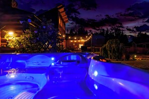Un área de hidromasaje con vistas a una casa y árboles de noche.