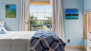Un dormitorio con techo de madera, una cama con manta estampada, una ventana con cortinas y dos cuadros en la pared.