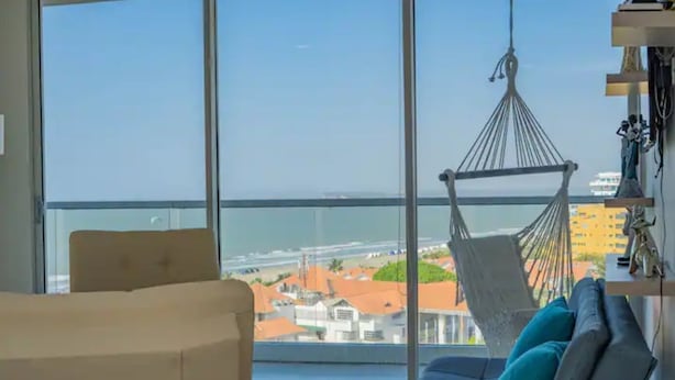 A room with a large window, a hammock, a sofa, and a chair.