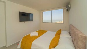 A bedroom with a bed, a TV mounted on the wall, and a window with a view.