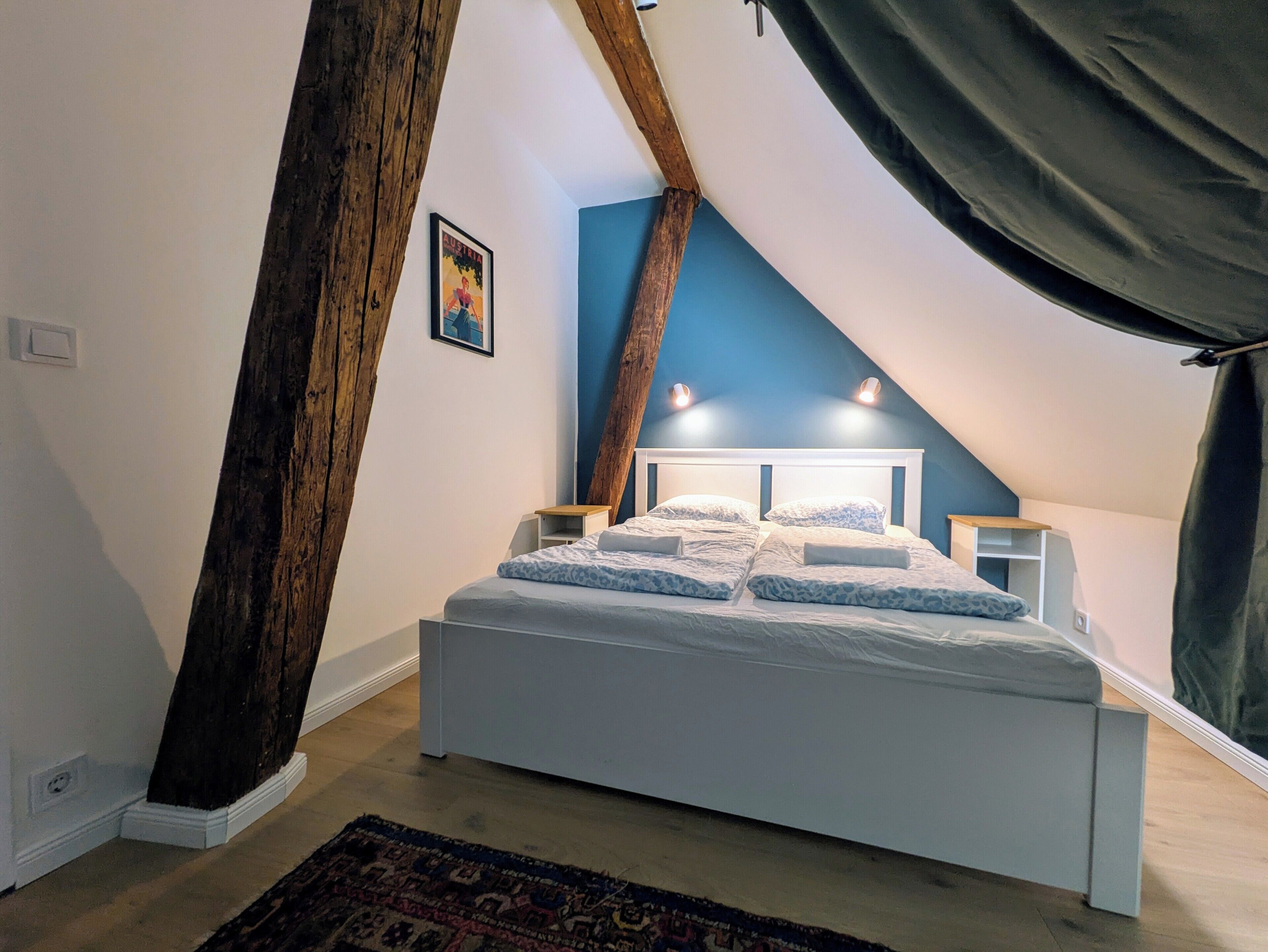 A bedroom with a sloped ceiling, a bed with white bedding, a patterned rug, and a framed picture on the wall.