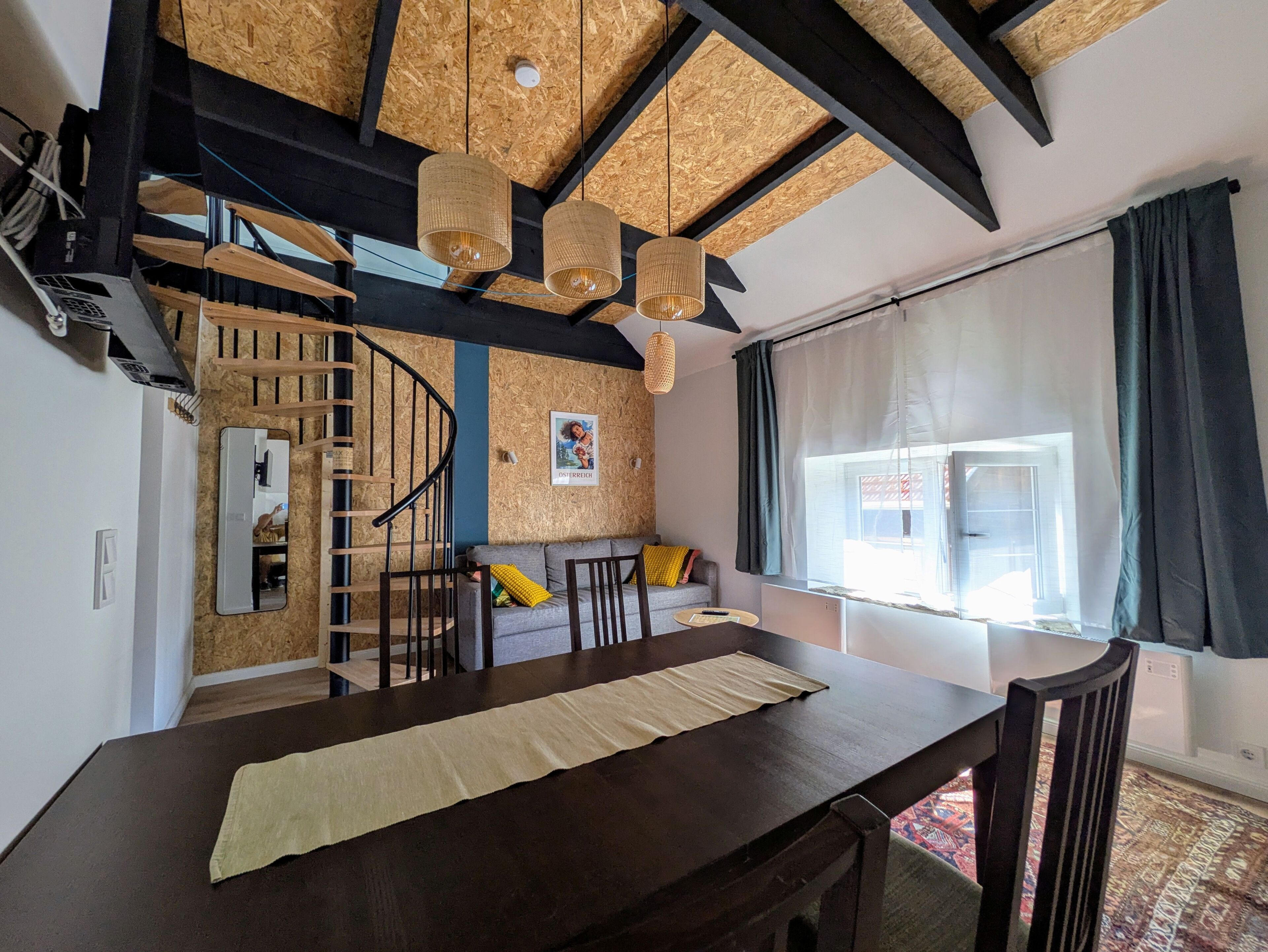 Uma área de refeições com mesa de madeira, cadeiras e escada que leva a um andar superior.