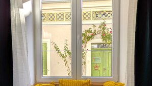 A window seat with yellow cushions and a blue cushion, overlooking a building with green doors and a yellow lattice design. - mg4 Apartments (Murau)