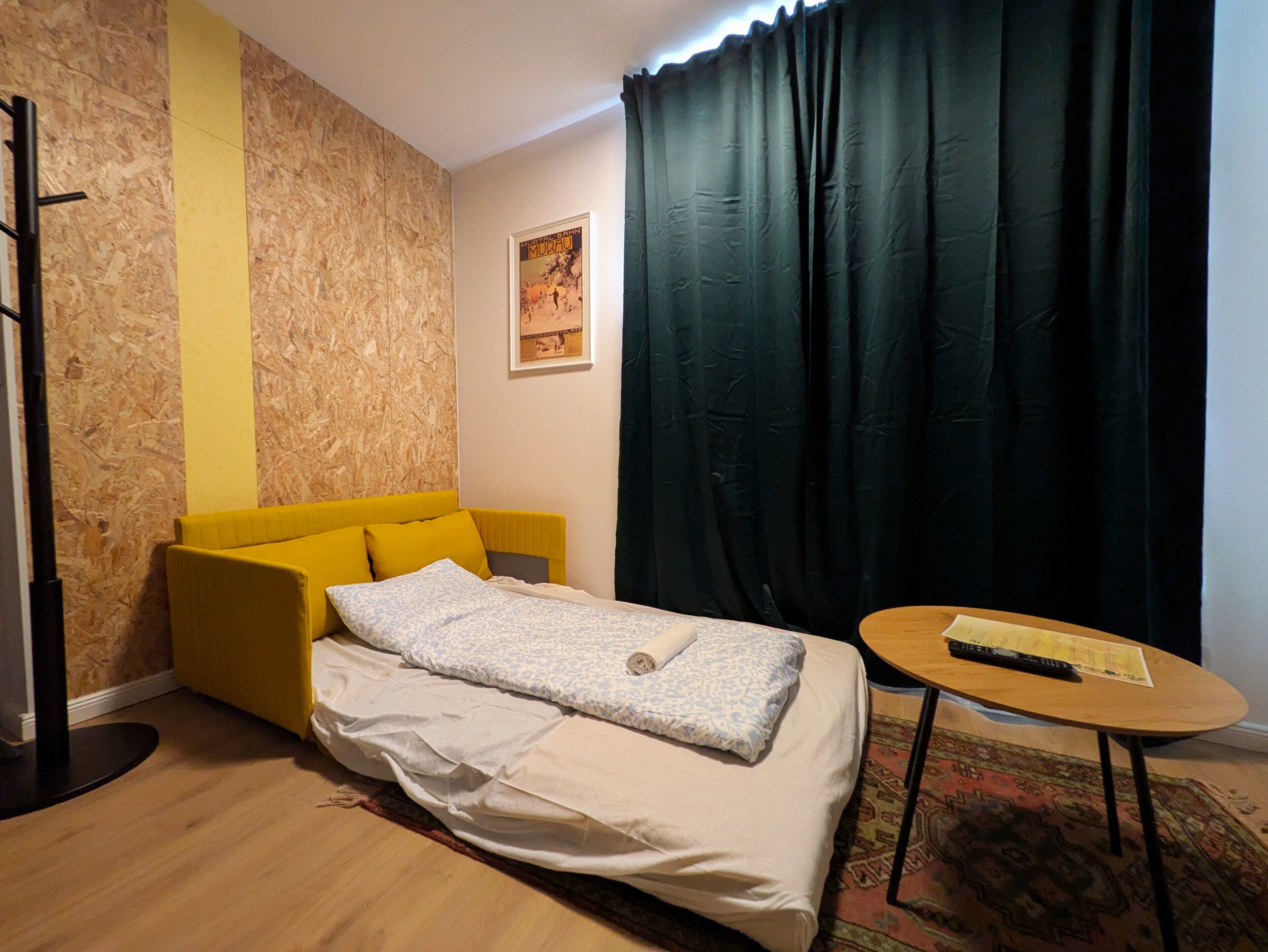 A bedroom with a bed, a small table, a chair, a curtain, and a poster on the wall.