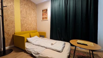 A bedroom with a bed, a small table, a chair, a curtain, and a poster on the wall.