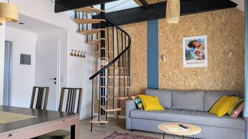 A modern living space with a wooden staircase, a grey sofa with colorful cushions, a round coffee table, and a patterned rug.