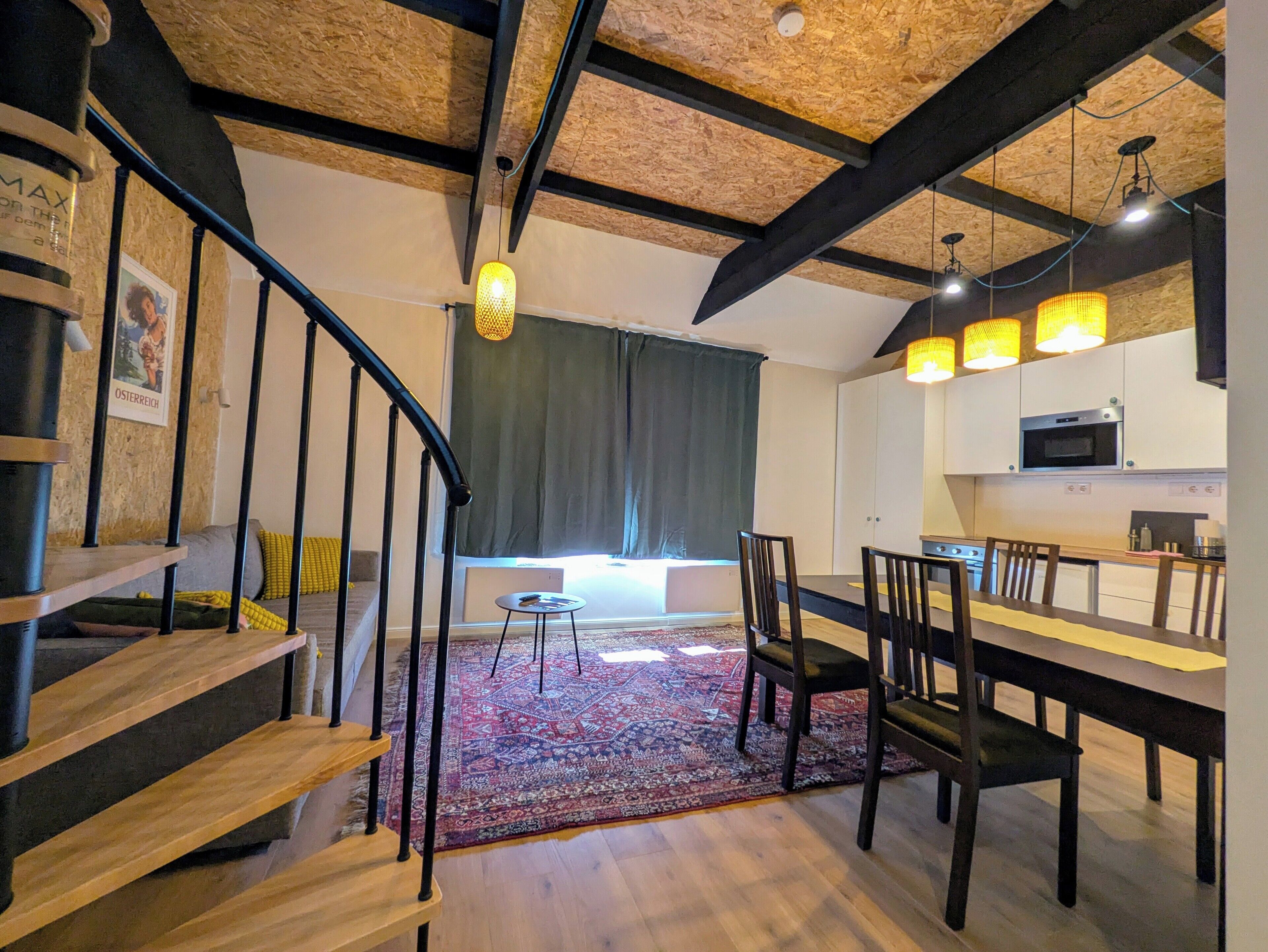 Un interior moderno con una escalera, comedor, cocina y un amplio ventanal con cortinas.