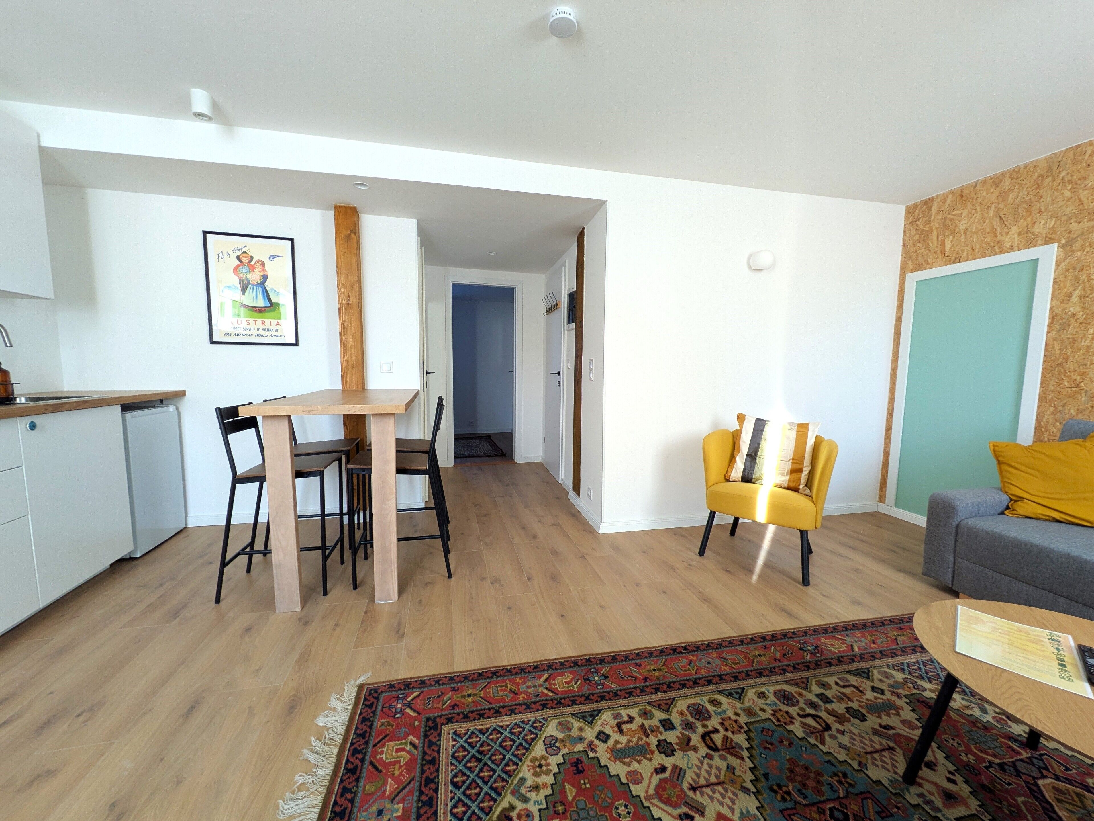 Een modern appartement met keuken, eetgedeelte en woonkamer. Er is een houten eettafel, stoelen, een bank en een vloerkleed met dessin.