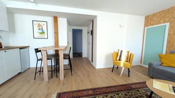 Een modern appartement met keuken, eetgedeelte en woonkamer. Er is een houten eettafel, stoelen, een bank en een vloerkleed met dessin.