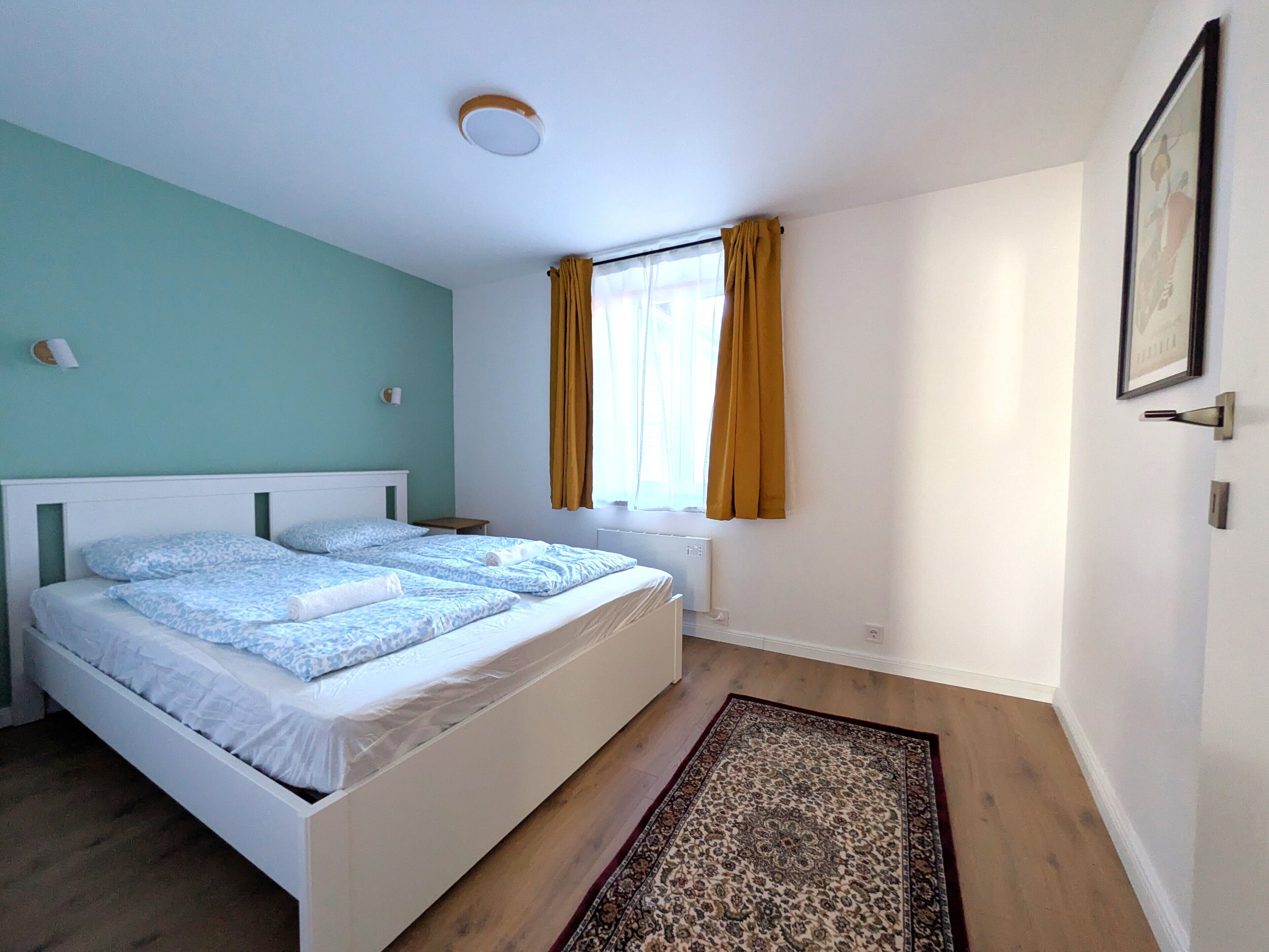 Un dormitorio con dos camas, una ventana con cortinas, un radiador y un cuadro en la pared.