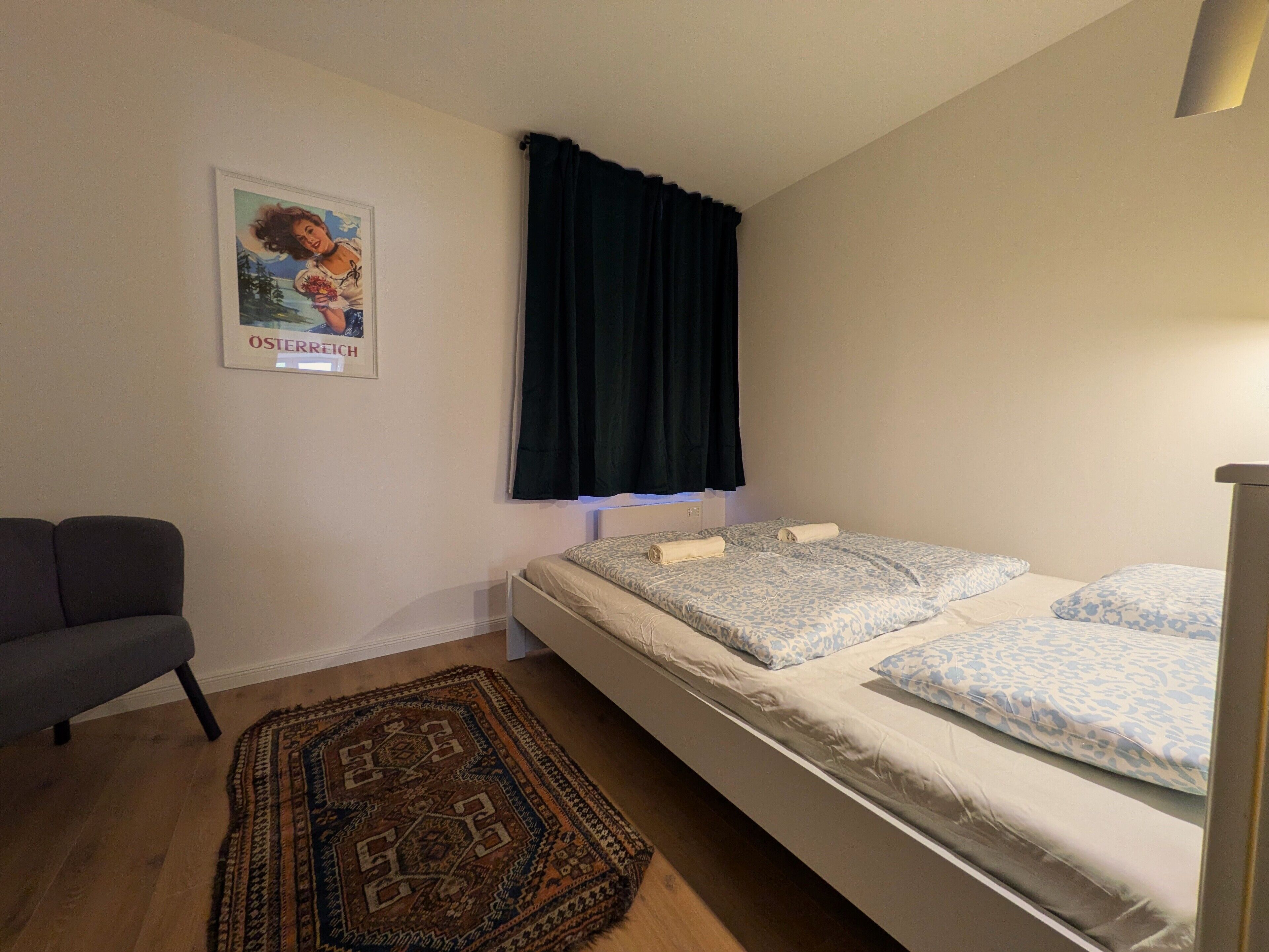 A bedroom with a bed, a chair, a poster, and a window with curtains.