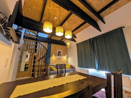 Una habitación con techo de madera, escalera de caracol, una mesa de comedor y un amplio ventanal con cortinas.