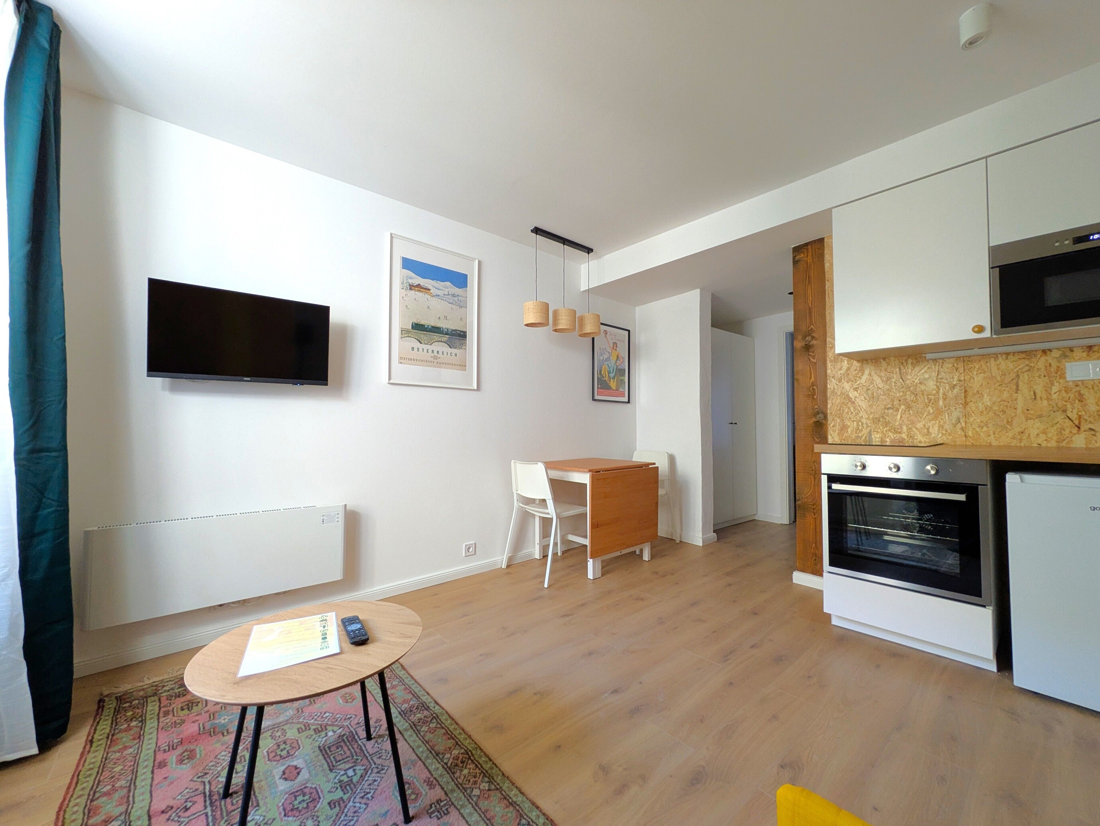 A modern kitchen with white cabinets, a built-in oven, and a microwave. There is a dining area with a white table and chairs, and a small rug on the floor.