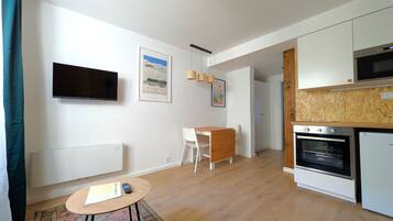 A modern kitchen with white cabinets, a built-in oven, and a microwave. There is a dining area with a white table and chairs, and a small rug on the floor.