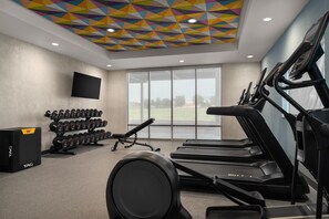 A gym with treadmills, dumbbells, and a TV on the wall.