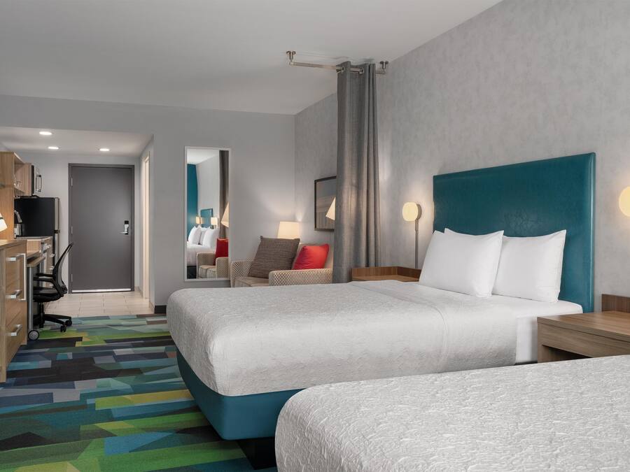 A hotel room with two beds, a desk, a chair, a television, and a bathroom visible in the background.