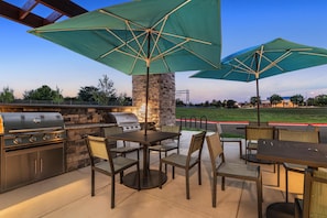 Un patio exterior con un muro de piedra, una parrilla y dos sombrillas que dan sombra.